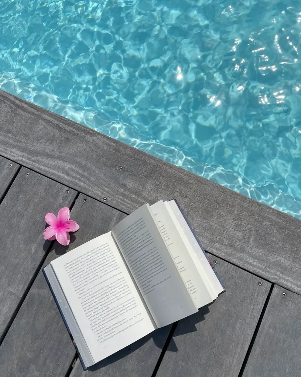 Livre ouvert et fleur rose au bord d’une piscine